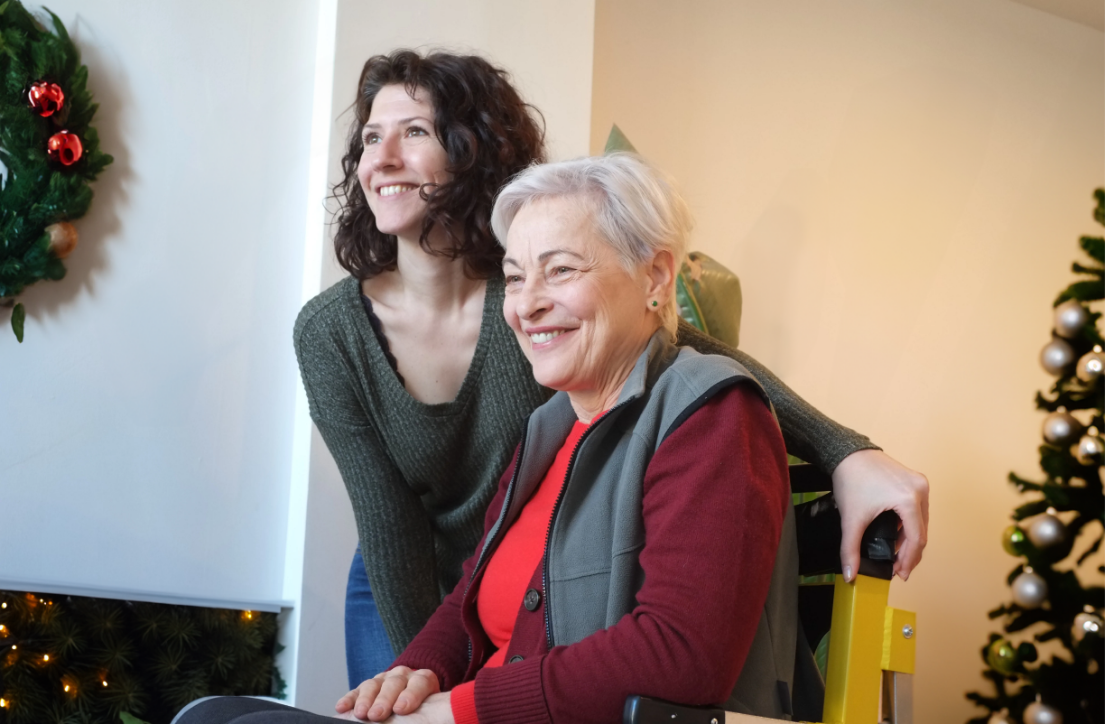 Two women smiling during the holidays while one uses a stair lift chair 